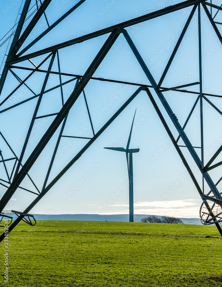 Fototapeta premium Wind Turbine seen through frame of an electricity pylon with blue sky