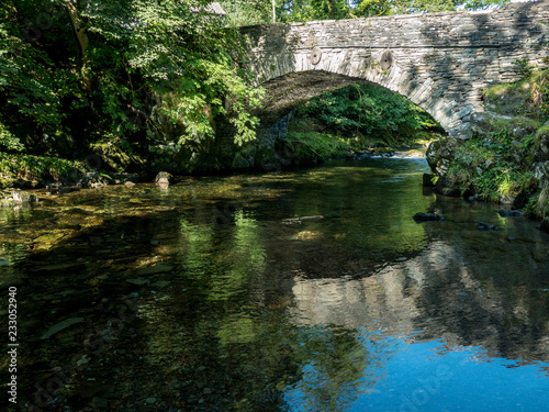 Stone Bridge over quiet stream in Elterwater with reflections and trees