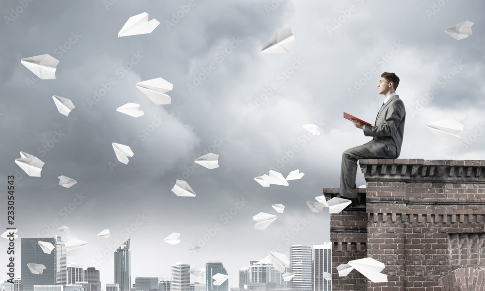 Man on roof edge reading book and cityscape at background Man on roof edge reading book and cityscape at background