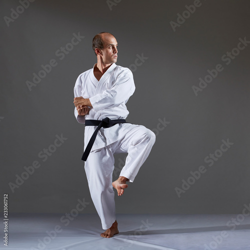 Tableau sur toile On a gray background, an active adult athlete performs formal karate exercises