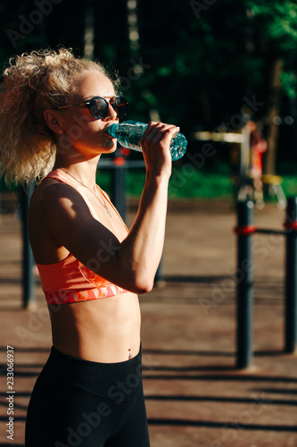 Photo of sports woman wearing sunglasses with bottle of water ne