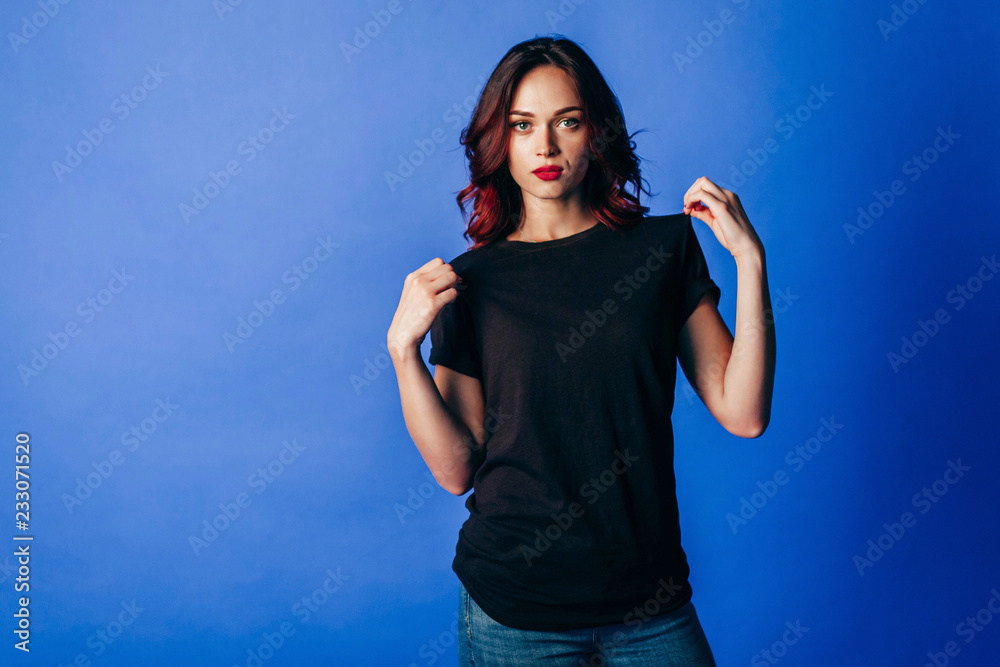 Beautiful young girl in posing in black t-shirt in the studio on blue background. Space for your logo Beautiful young girl in posing in black t-shirt in the studio on blue background. Space for your logo