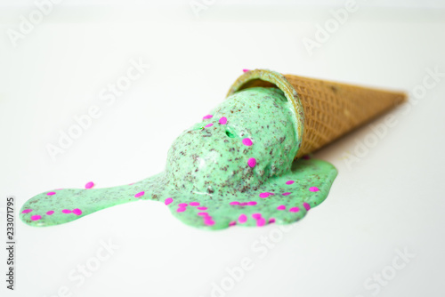 Ice cream cone. mint chocolate chip, peppermint bon bon ice cream with pink sprinkles in a waffle cone laying on side melting on white background. 