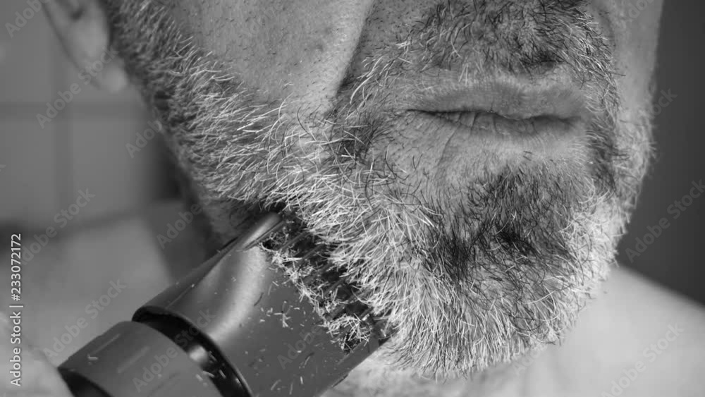 Shaving the beard on the chine area of the man using the black shaver in a black and white background