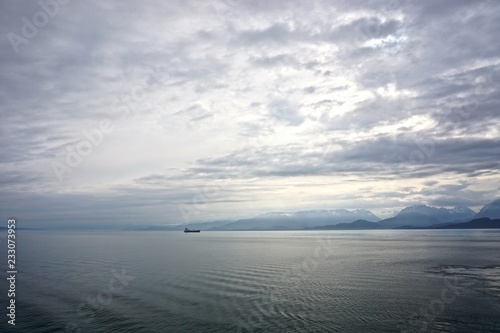Cook Inlet, Alaska, USA: A freighter on the horizon against mountains shrouded in morning mist, with dense, dramatic clouds overhead.