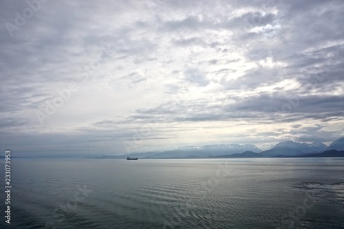 Cook Inlet  Alaska  USA  A freighter on the horizon  against mountains shrouded in morning mist  with dense  dramatic clouds overhead.