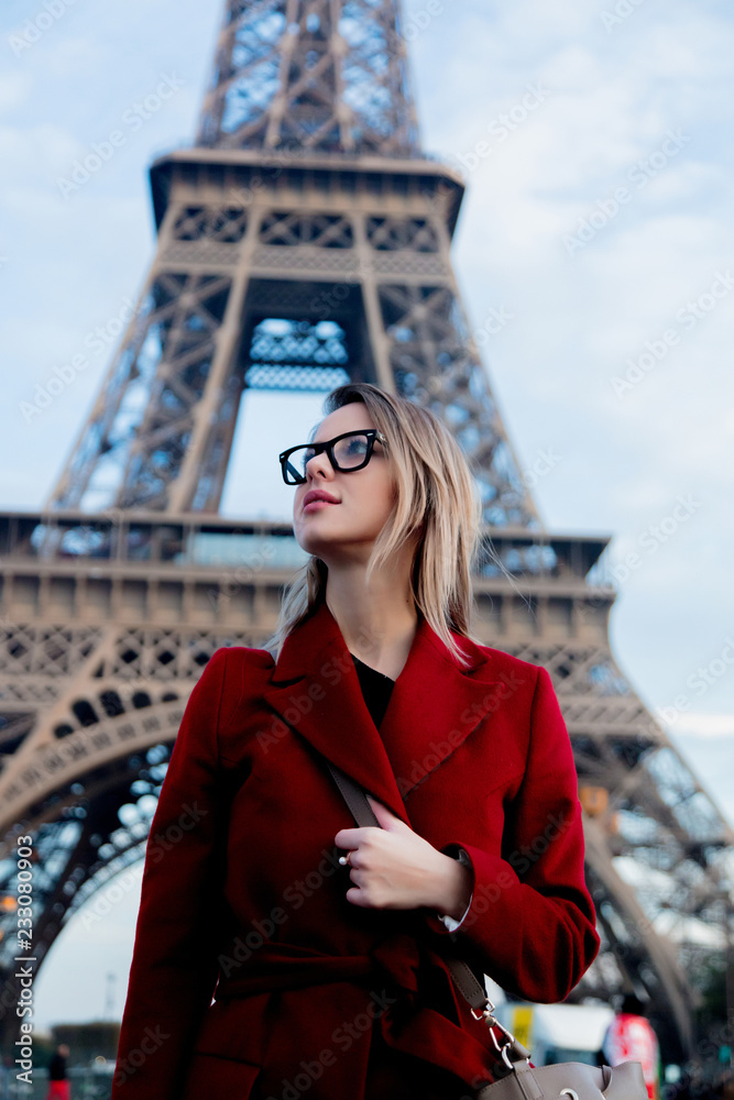 Style redhead girl in red coat and bag at parisian street with view at Eiffel tower in autumn season time