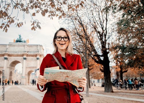 Style redhead girl in red coat and bag with map in parisian park in autumn season time