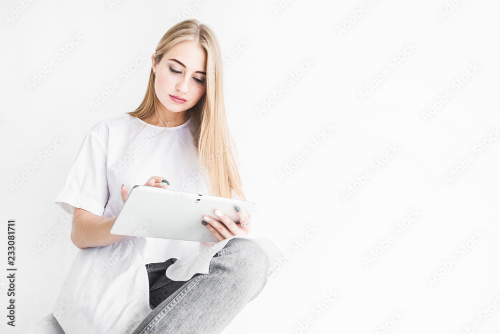 Portrait of a young stylish blonde girl in a white T-shirt and blue jeans using a tablet on a white background Portrait of a young stylish blonde girl in a white T-shirt and blue jeans using a tablet on a white background