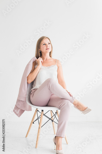 Portrait of a young blonde girl sitting on a chair against a white wall and holding a jacket in her hands © xartproduction