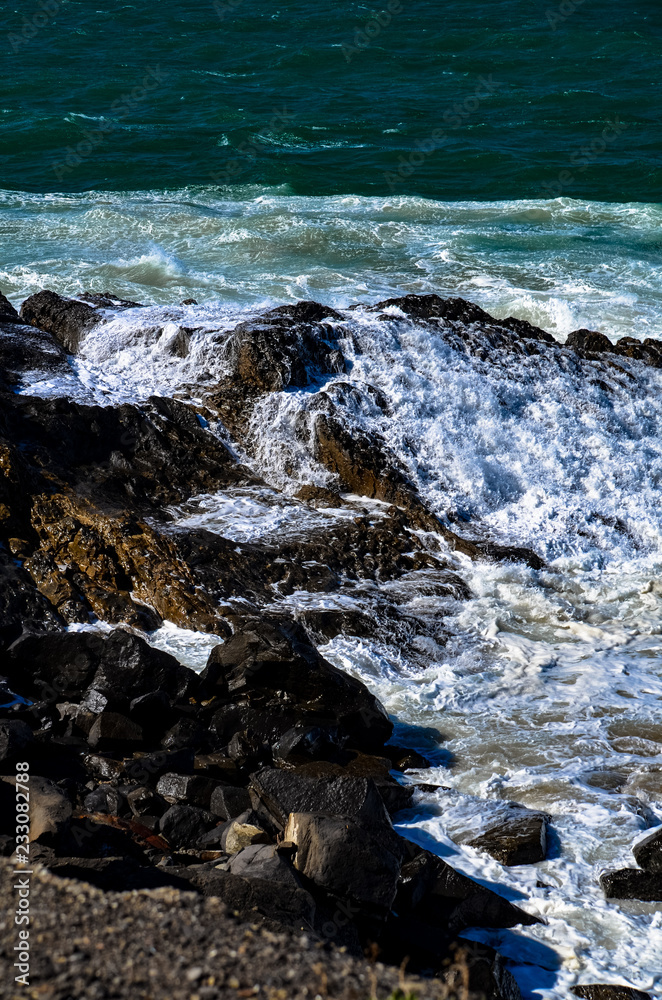 Pacific Ocean waves crashing into a rock formation at Mugu Rock in Malibu, California