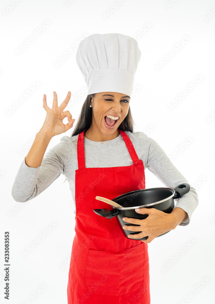 Beautiful young woman chef with wooden spoon, pot red apron and hat making a great ok gesture