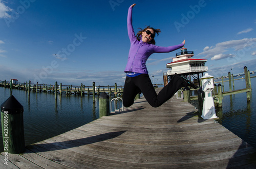 Beautiful woman jumps on a dock alongside the Choptank River Lighthouse in Maryland photo