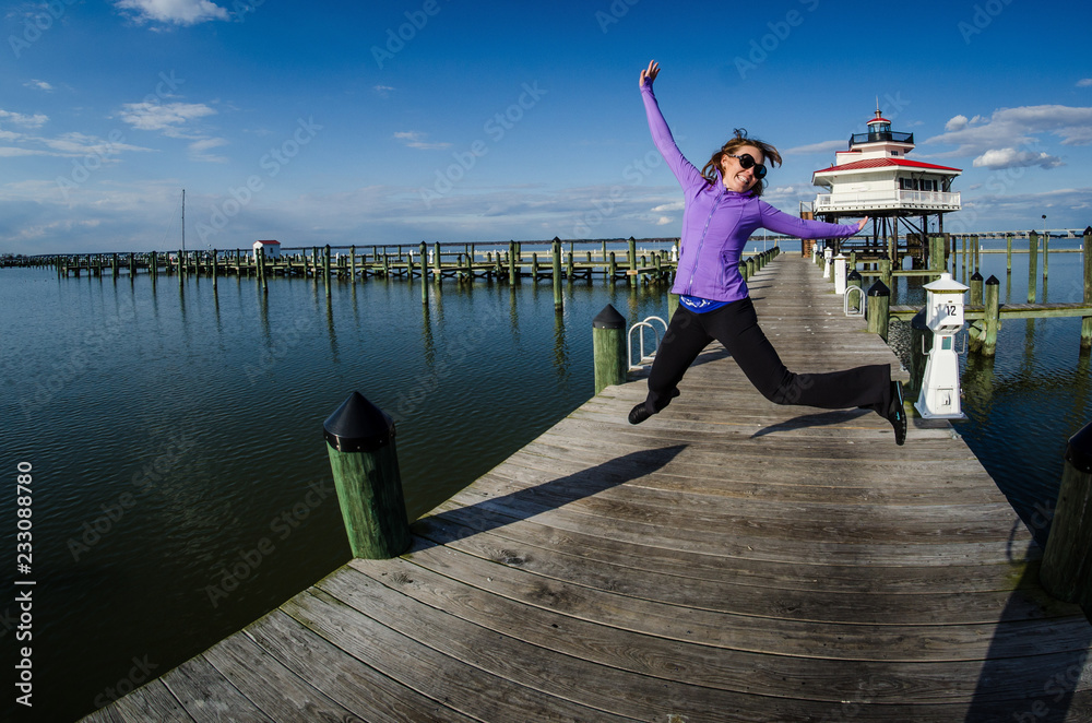Beautiful woman jumps on a dock alongside the Choptank River Lighthouse in Maryland