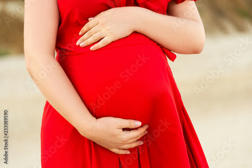 Pregnant women standing on the beach and touching her belly