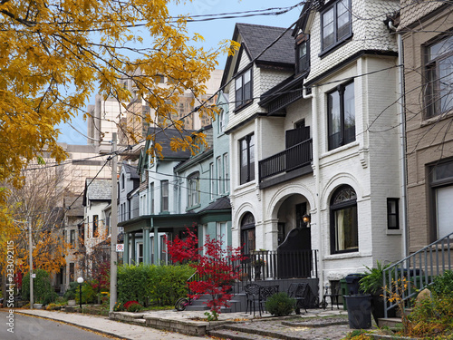 street of historically designated old Victorian houses with gables and painted brick  downtown Toronto  with large office building in background