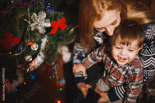 Mother and child sitting beside Christmas tree at home