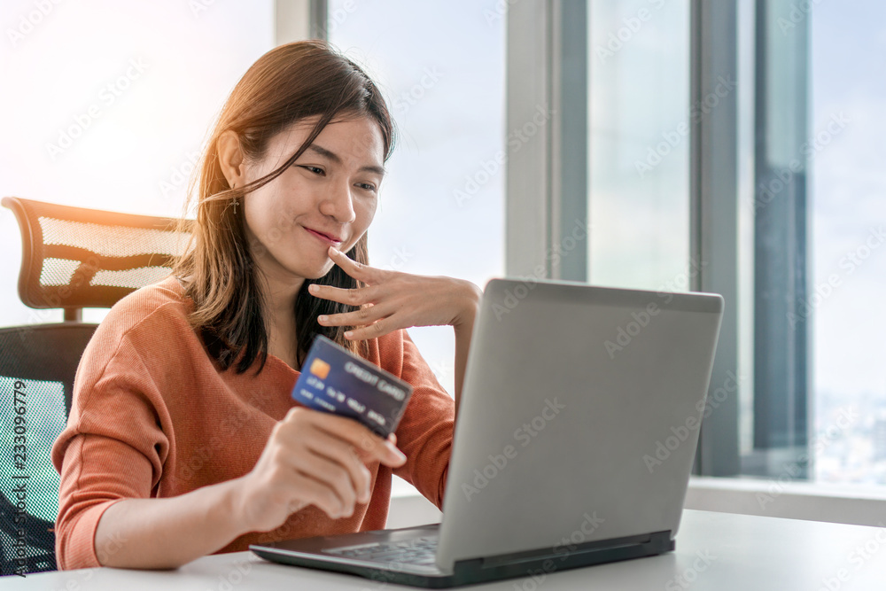 Young asian woman holding credit card and use laptop for purchase product on internet in home office, Cyber Monday shopping online concept, Copy space. Young asian woman holding credit card and use laptop for purchase product on internet in home office, Cyber Monday shopping online concept, Copy space.