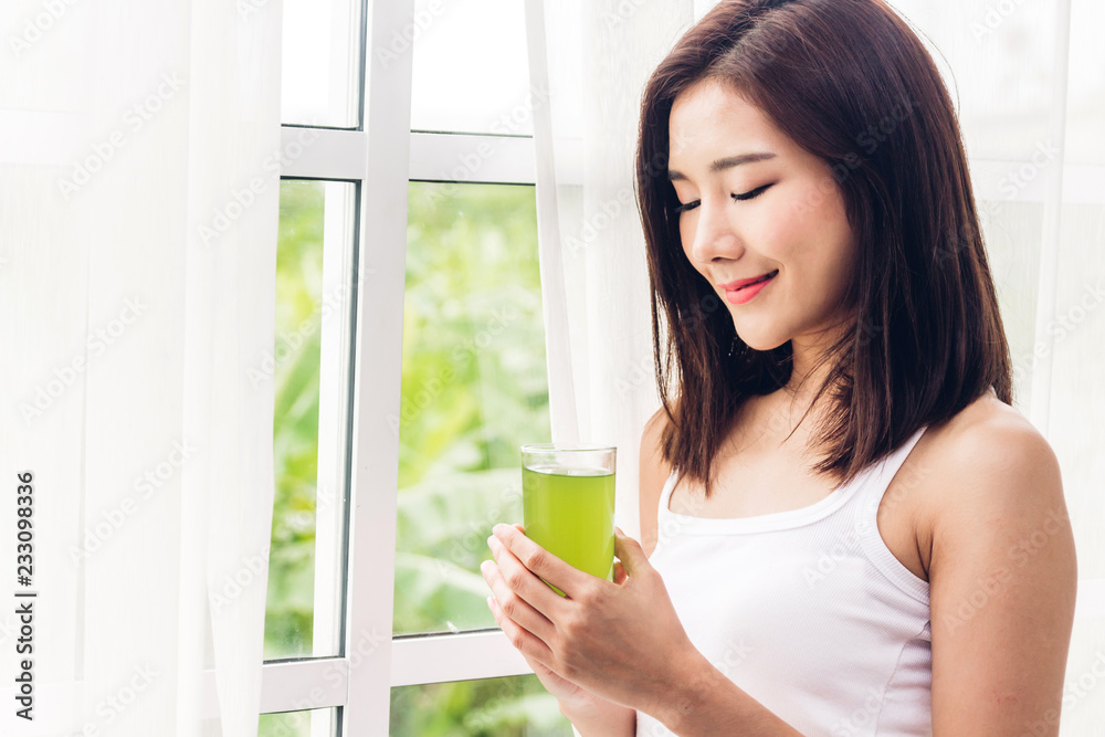 Woman enjoy healthy drinking green detox vegetable juice near window curtains in the living room at home.dieting concept.healthy lifestyle Woman enjoy healthy drinking green detox vegetable juice near window curtains in the living room at home.dieting concept.healthy lifestyle