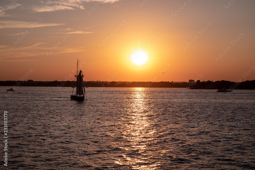 Scenic view of a small sailboat at a sunset in a city harbor. Sun rays left beautiful sunpath on a water