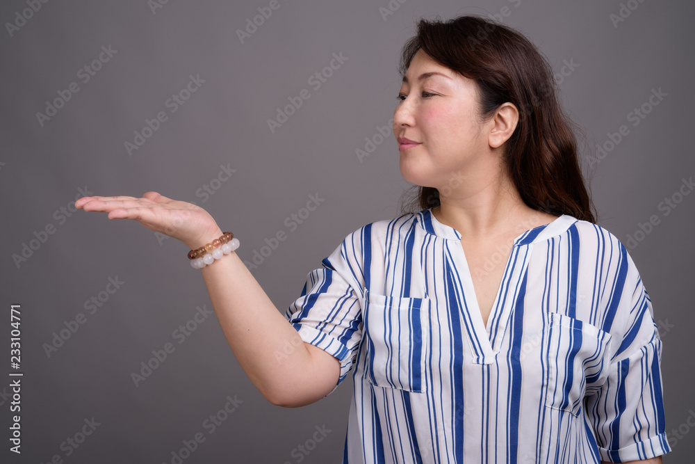 Mature beautiful Asian businesswoman against gray background Mature beautiful Asian businesswoman against gray background