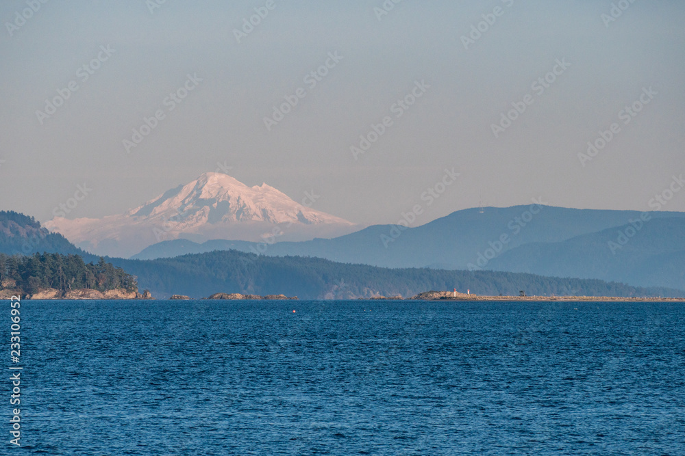 blue ocean under blue sky with snow caped mountains behind island  in the background