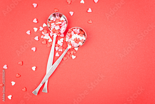 Pair of spoons with sweet hearts-confetti on a red background.