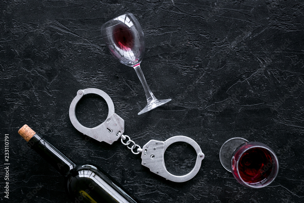 Illegal sale of alcohol concept. Handcuffs near wine glass and bottle on black background top view space for text Illegal sale of alcohol concept. Handcuffs near wine glass and bottle on black background top view space for text