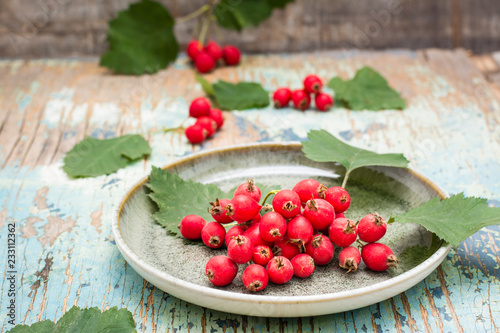 A handful of hawthorn berries with leaves on a plate on a rustic background