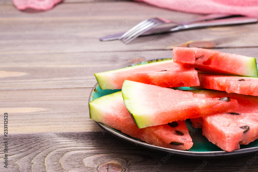 Sliced watermelon on a ceramic plate, cutlery and napkin on a wooden table. Copy space