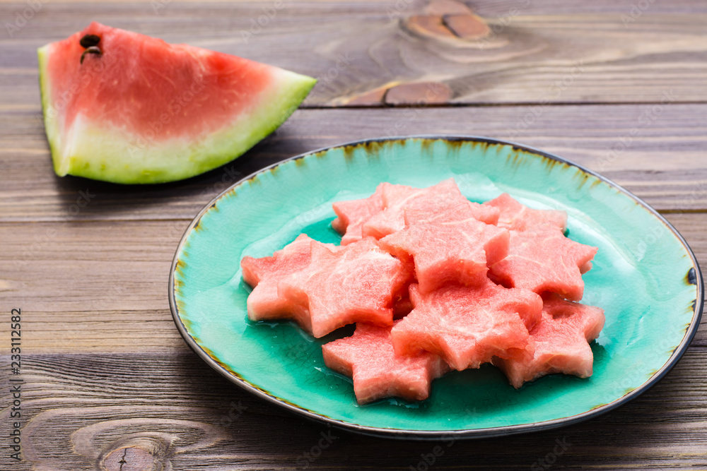 Pieces of watermelon in the form of stars on a ceramic plate and a large piece of watermelon on a wooden table