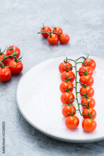 Ripe honey cherry tomatoes on a branch on a plate on a concrete background