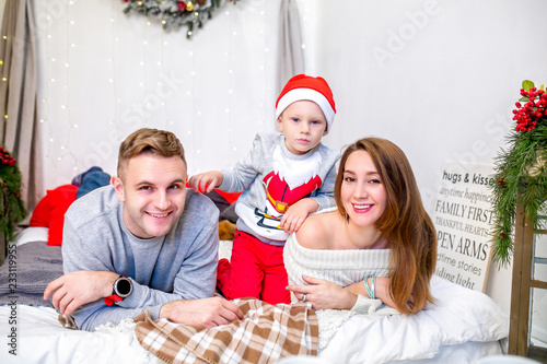 Happy family  father  mother and son  in the morning in bedroom decorated for Christmas. They open presents and have fun. New Year s and Christmas theme. Holiday mood