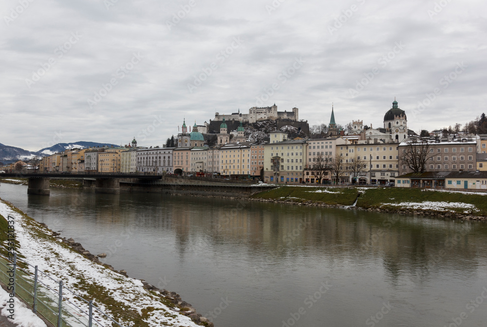 panoramic winter view of the historic center of Salzburg Austria surrounded by the Alps covered with snow in a foggy haze from the bridge with padlocks