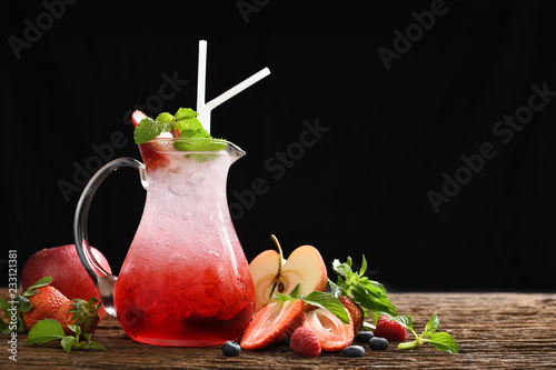 Mixed fruit juice with syrup and soda in glass pitcher surrounded by fruits on wooden background