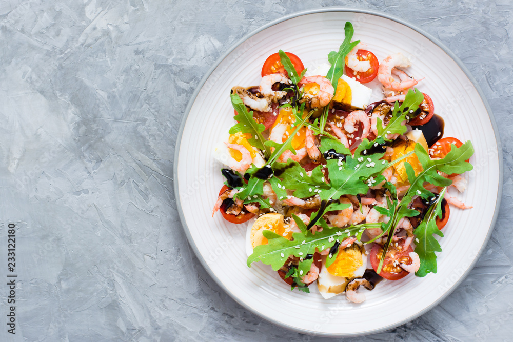 Appetizing salad of cherry tomatoes, eggs, boiled shrimps, arugula, sesame seeds and balsamic sauce in a plate on the table. Top view Appetizing salad of cherry tomatoes, eggs, boiled shrimps, arugula, sesame seeds and balsamic sauce in a plate on the table. Top view