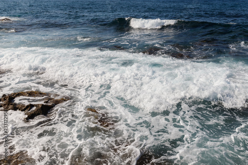 sea waves are broken by splashes and white foam on huge rocks in the warm Mediterranean sea in which boats and yachts