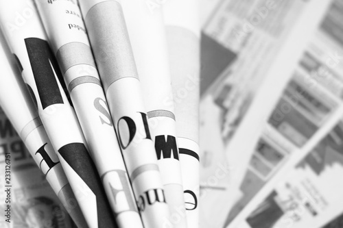 Folded newspapers with partially visible headlines against background of pages with articles - blurred text and photos. Daily papers with news, business and finance journals at the office, fresh press