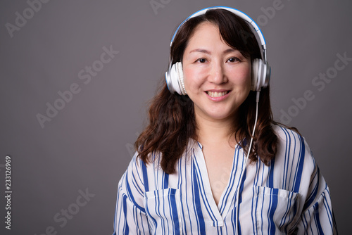 Mature beautiful Asian businesswoman listening music with headphones