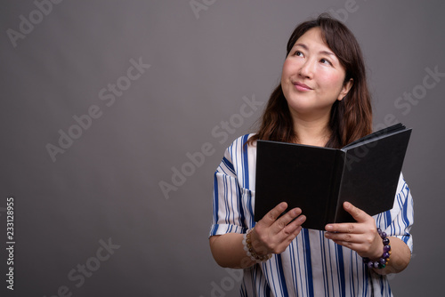 Portrait of mature beautiful Asian businesswoman reading book