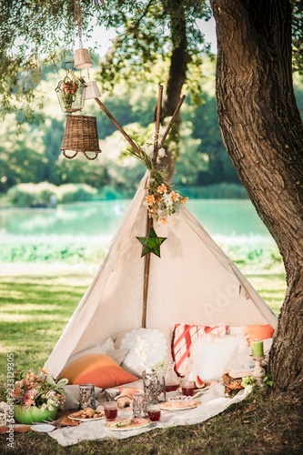 Romantic picnic in open-fronted teepee under tree in idyllic summer landscape photo