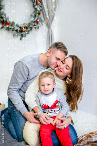 Happy family, father, mother and son, in the morning in bedroom decorated for Christmas. They hug and have fun. New Year's and Christmas theme. Holiday mood