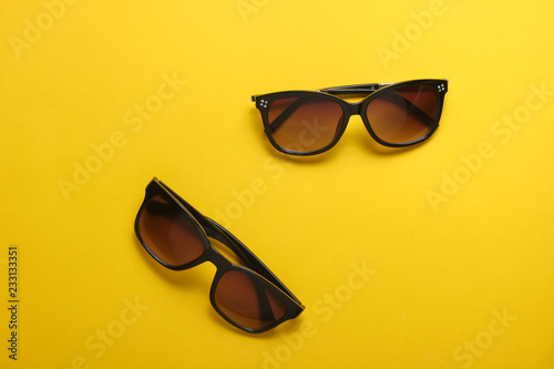 Two pairs of fashionable.sunglasses on yellow background. From above, minimalism.