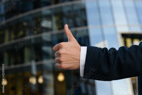 Businessman in a suite is holding big thumb up. Close up. Copy space