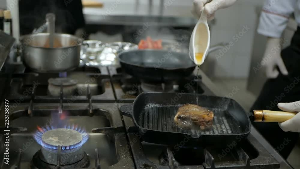 Chefs cooks and doing flambe on beef steak in grill pan in restaurant kitchen Chefs cooks and doing flambe on beef steak in grill pan in restaurant kitchen