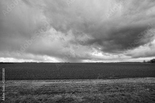 Flat Dutch polder landscape in black and white with rolling thunder clouds and agricultural land.
