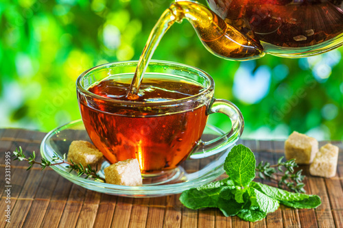 Tea time. Pouring out hot tea into a cup. Green nature background.