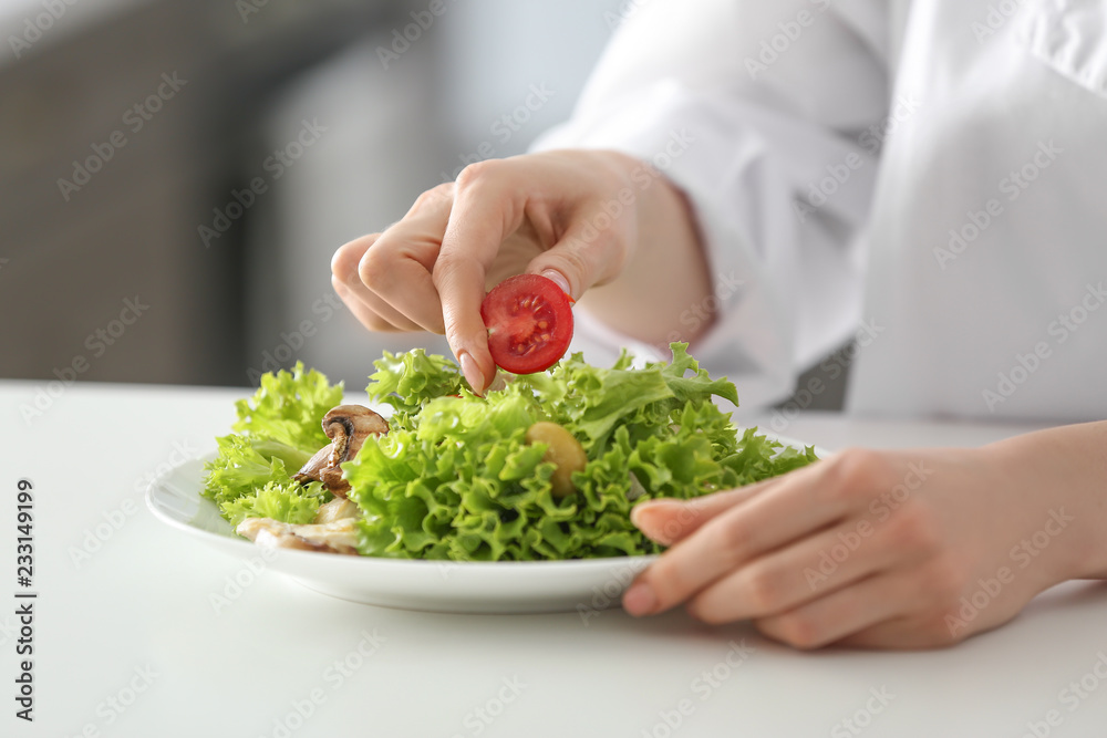 Young female chef preparing tasty salad in kitchen, closeup