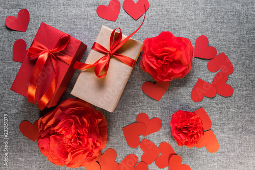 the gift box is wrapped in a red ribbon, and with paper hearts and flowers around, on a gray background