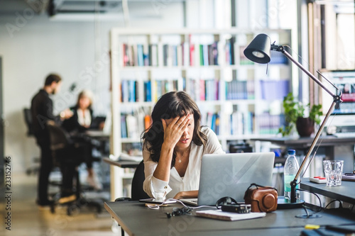 Tired businesswoman leaning by laptop on desk in creative office
